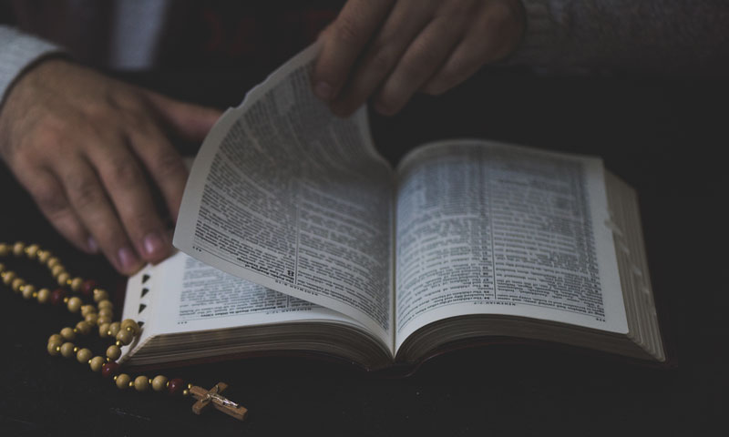 An open Bible with a hand turning the page.